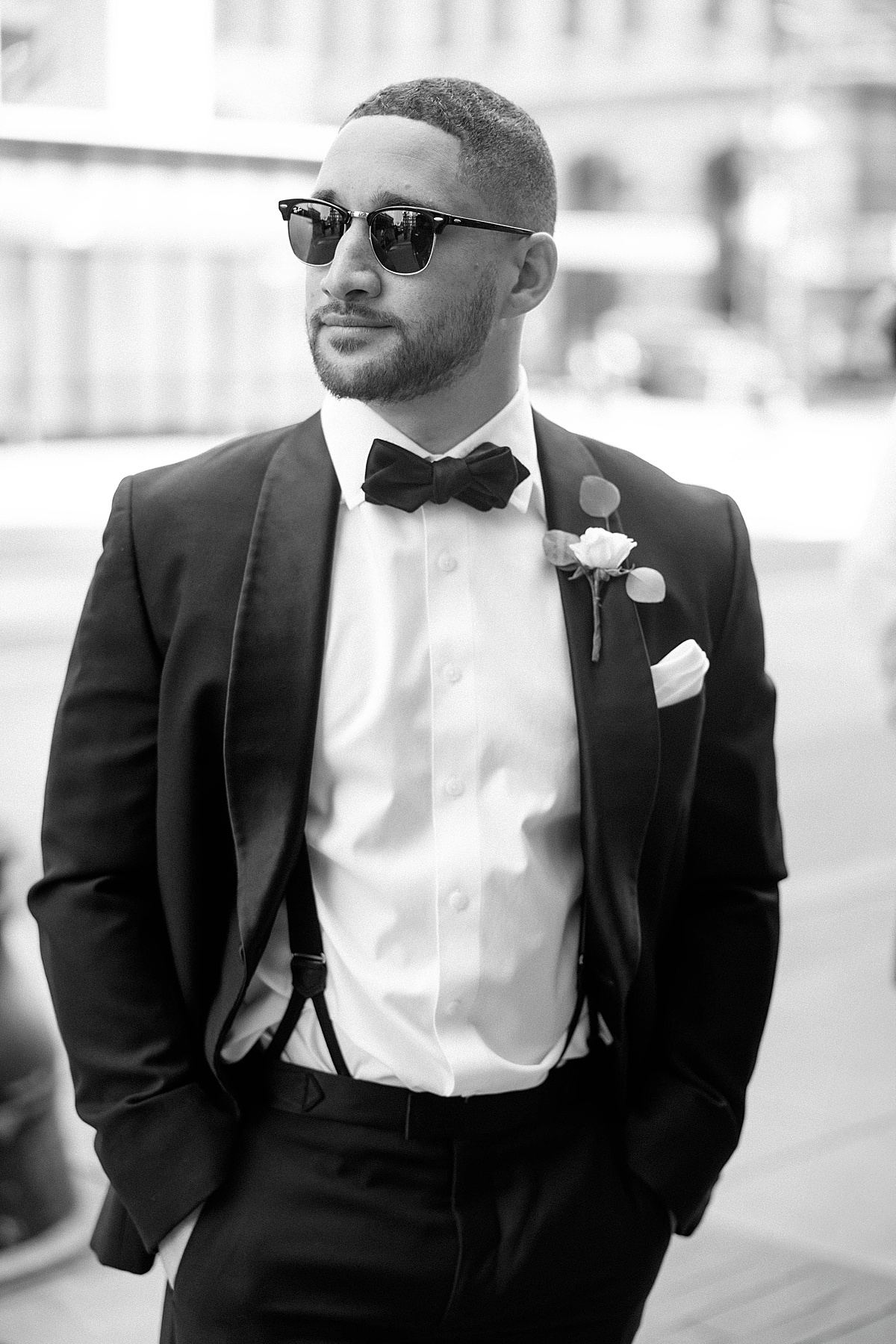 Groomsman in tuxedo and sunglasses looking down the street in front of the Loews hotel in Philly by Kristy Hoadley