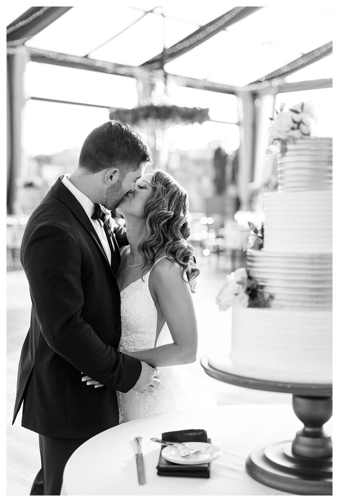 Couple kissing by cake at Cescaphe Waterworks wedding reception